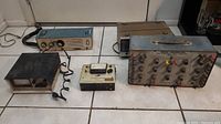 Five electronic devices including Heathkit GW-11 CB transceiver, various analog testing and radio units on tiled floor.