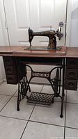 Front view of the 1923 Singer sewing machine mounted on the wooden cabinet with cast iron treadle base, showcasing the decorative gold detailing and drawer storage.