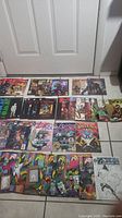 Photo of assorted 45 comic books laid out on a tiled floor showing various cover arts and titles.