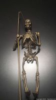 Full front view of bronze skeleton sculpture holding scythe on black background