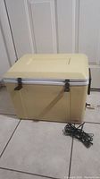 Closed view of Koolatron P34A cooler/warmer showing beige body, cream lid, black latches and handle, with power cord coiled beside it.