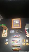 Photo showing framed Distinguished Marines stamps and various medals, ribbons and coins laid out on black surface.