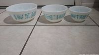 Three white glass Pyrex mixing bowls with turquoise Amish Butterprint design, arranged largest to smallest