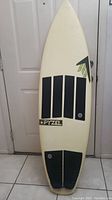 Surfboard standing facing front, showing white deck with black traction pads and Pyzel logo