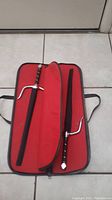 Two steel sai in an open red carrying case with individual compartments and black lining.