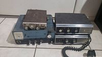 Three CB radios placed side by side showing Knight KN2560 with blue panel below two Hallicrafters CB-5 units with dark and silver finish, one Hallicrafters unit connected to coiled mic cord.