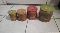 All four vintage collectible tins shown in a row on tile floor.