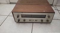 Front three-quarter view showing wood veneer cabinet top and metal faceplate with control knobs