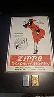 Full view of vintage Zippo metal sign with woman illustration and two lighters below it, one silver-tone and one gold-tone.