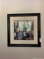 Framed art print shown hanging on a wall, depicting wine bottles and a wine glass, with a black frame and gold accents.