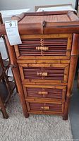 Front view of bamboo cabinet showing four drawers with bamboo slats and rattan panels and bamboo latch handles.