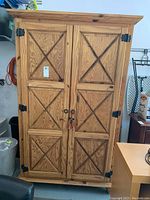 Full view of cabinet front showing wood panel doors with X design, black metal hinges, and round door pulls.
