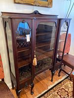 Front view of dark wood display cabinet with glass shelves and decorative wooden carvings.