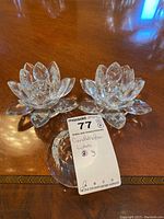 Two lotus flower shaped crystal candle holders on a wooden table, one missing a glass petal.