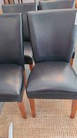 Four black faux leather parson chairs with wooden legs arranged on a woven rug, showing condition and style