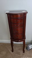Front view of the tall wooden jewelry box cabinet with five drawers and carved column details on the sides.