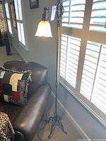 Full view of the brass-colored floor lamp with glass shade beside a couch by a window, showing the lamp lit and its overall height and design.