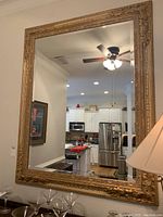 Full view of the mirror mounted on a wall reflecting a kitchen area and ceiling fan.