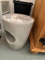 Full view of a gray concrete plant stand showing scratches on the top surface and a curved cutout in the middle.
