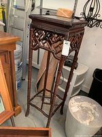 Full view of tall wooden plant stand with bamboo style design and carved feet from an angle showing the lattice sides.
