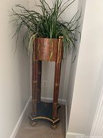Full view of the wooden plant stand with faux grass in woven basket planter, showing the entire piece against a corner wall.