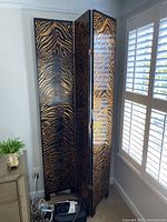 Wooden folding room divider composed of three panels with a black and gold zebra print.