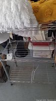 Full view of the three-tier wire shelf with visible contents behind it, showing the metal wire shelves and vertical supports.