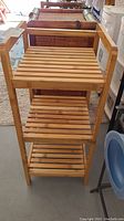 Front view of the wooden shelf showing three slatted shelves with a light wood finish.