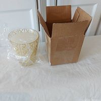 Photo showing the candle wrapped in plastic next to the brown cardboard box it came in.