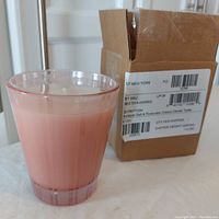 Nest New York scented candle in pink glass holder, with candle removed from plain cardboard box showing label with scent and weight information.