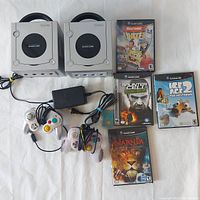 Two silver Nintendo GameCube consoles, four games in cases, two controllers, one power cord, and one memory card laid out on a white surface.