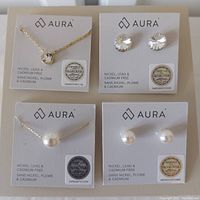 Photo showing all four jewelry items on Aura branded cards with Swarovski holographic stickers: two pairs of earrings and two matching necklaces, one set with clear crystals and one with pearls.
