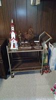 Full view of the metal frame bar cart showing two shelves, wood handle, and caster wheels, with various items placed on the top shelf (not included).