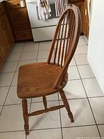 Side view of one oak dining chair showing the curved spindle back, turned legs, and seat profile.