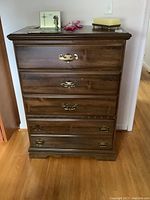 Front view of six drawer wood dresser showing dark wood finish and brass handles.