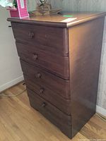 Front side angled view of vintage wooden dresser showing five drawers with round knobs.