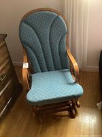 Front view of wood framed glider chair with blue upholstery featuring subtle diamond and floral pattern.