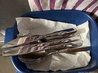 Loose flatware pieces in a blue container on paper towel showing shine and design