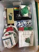 Top down view of plastic bin showing assorted cloth napkins, disposable plates with poinsettia designs, and boxed disposable napkins.