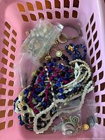 Plastic pink bin containing assorted bead necklaces and small ziplock bags of pins and earrings