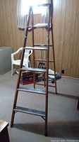 Full view of wooden step ladder standing open with visible paint marks and wear on steps and shelf