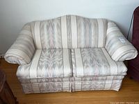 Front view of the upholstered love seat showing fabric pattern, zippered cushions, and overall shape.
