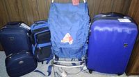 Five luggage pieces arranged together in a row: three suitcases, one large backpack, and a smaller bag. Different brands visible including Heyes, B International, and Air Born.