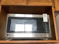 Front view of LG stainless steel microwave oven in a wooden shelf, showing digital control panel and door.