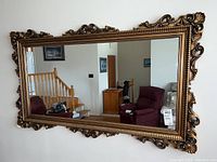 Full view of the large rectangular mirror showing the ornate metallic composite frame and part of the interior room reflected in the glass.