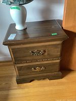 Night table showing front with two drawers and brass-tone handles, one handle missing.