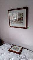 Two framed prints by Trisha Romance shown, one hanging on wall, one laying on mattress.