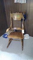 Full front view of oak rocking chair with pressed back design and spindle backrest, showing wood grain and armrests.