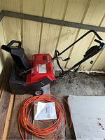 Side view of the Noma electric snow thrower with extension cord coiled on the floor and instruction manual placed beside it.