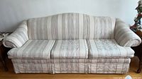 Front view of the three seat sofa showing striped fabric upholstery with a skirted base and three seat cushions with visible zippers.